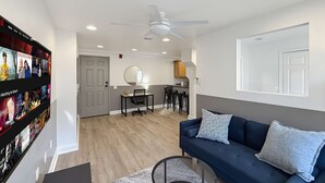 A modern living room with a dark blue sofa, a round coffee table, and a wall-mounted TV displaying movie options.