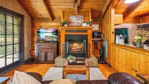 Un salon chaleureux avec une cheminée, des murs en bois, un téléviseur et un coin salon confortable.