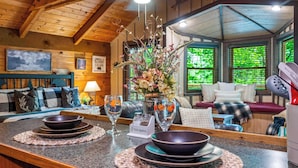L’intérieur chaleureux d’un chalet avec un plafond en bois, un coin repas avec une table dressée pour deux personnes et un salon doté d’un canapé et d’une cheminée.