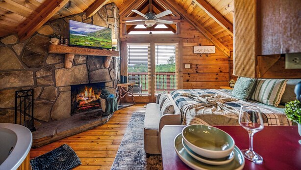 A cozy cabin interior with a stone fireplace, wooden ceiling, and a comfortable seating area. - Hot Tub! Cute Studio Cabin! Views! Private! Relax! (Sevierville)