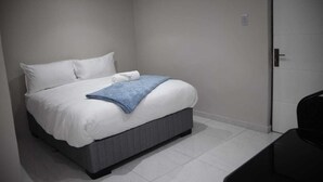 Un dormitorio moderno con cama, ropa de cama blanca, una manta azul y un cabecero gris.