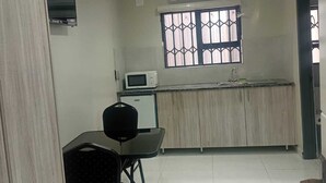Una cocina compacta con microondas, un refrigerador pequeño, una ventana con barandillas decorativas y un área de comedor con una silla y una mesa.