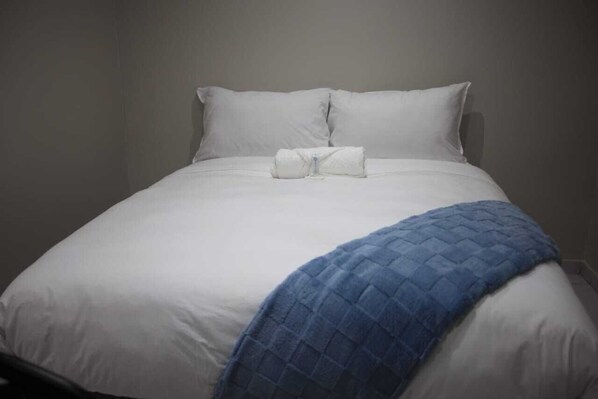 A neatly made bed with white linens and a blue blanket, pillows, and a folded towel on the bed. - Hayat Hotel 94Juta (Johannesburg)