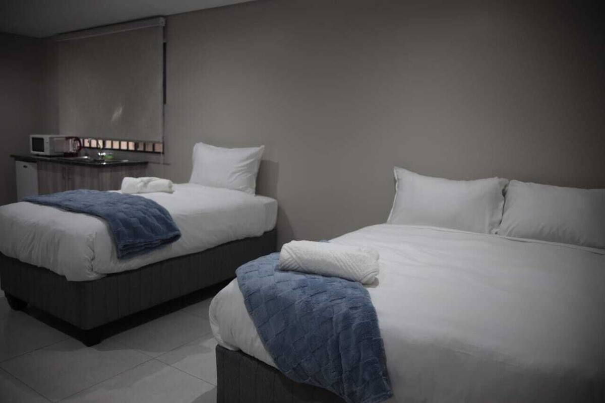 Two single beds with white linens and blue blankets, a small kitchenette with a microwave, and a mirror on the wall.