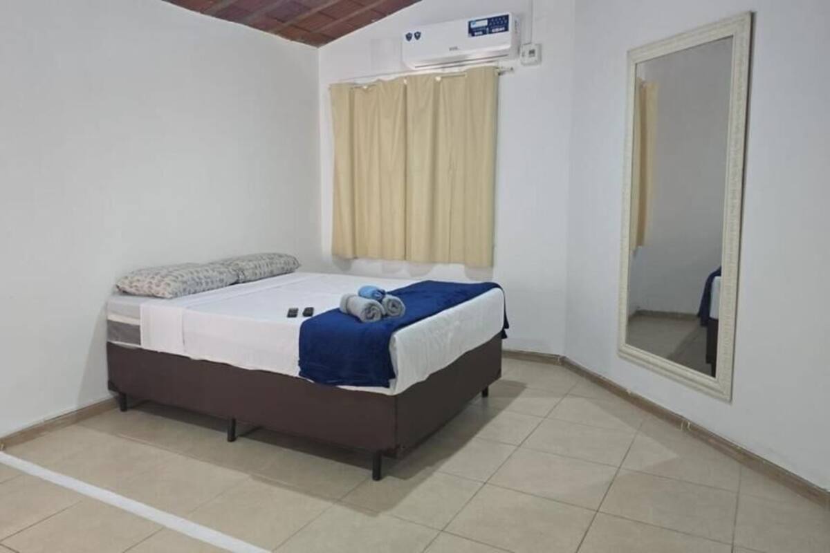 Una habitación pequeña y limpia con una cama individual, un espejo y una ventana con cortinas.