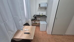 A small kitchenette with a microwave, a sink, and a refrigerator. There is a table with a remote control and a water bottle. - 360 Casa Praia Botafogo By SUHCasa (Rio de Janeiro)