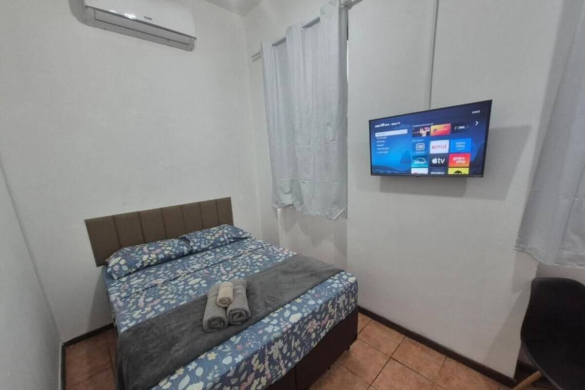 Un dormitorio con una cama, un televisor montado en la pared y una silla.