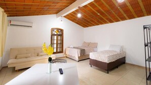 A room with a wooden ceiling, two beds, a sofa, a table with a vase of flowers, and an air conditioning unit. - 360 Casa Praia Botafogo By SUHCasa (Rio de Janeiro)