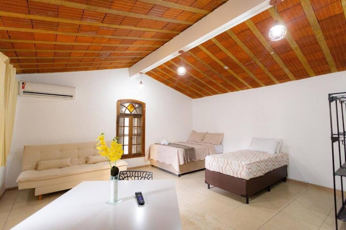 Una habitación con techo de madera, dos camas, un sofá, una mesa con un jarrón de flores y un equipo de aire acondicionado.