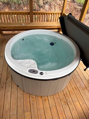 Ein Whirlpool auf einer Holzterrasse mit einem Holgitter im Hintergrund.