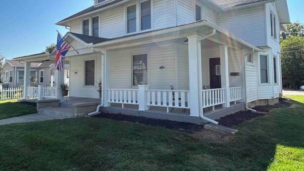 A two-story house with a front porch, a flag, and a well-maintained lawn. - London Maisonette: Black Door
• Great space in a small town close to a big city! (London)