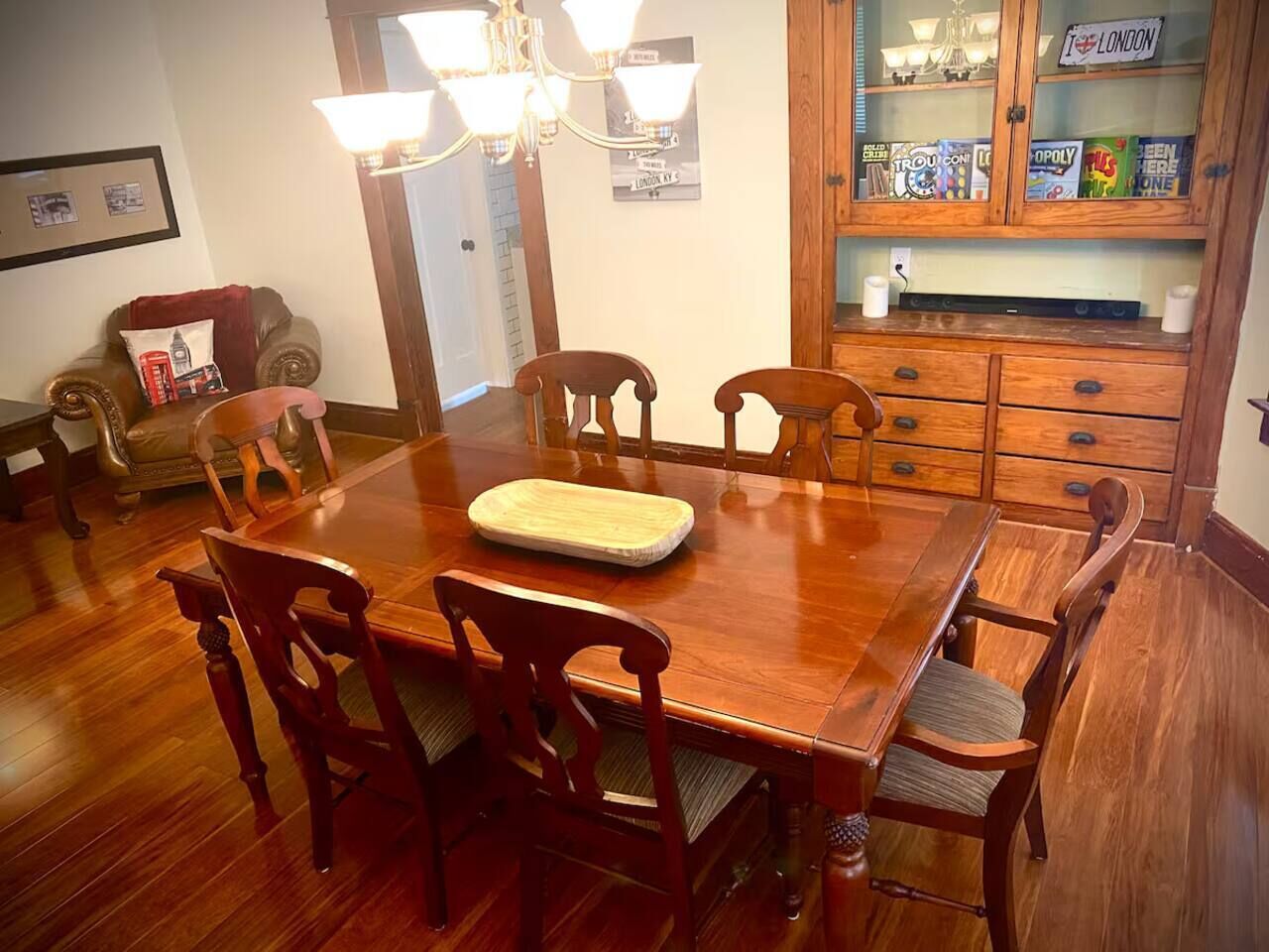 Une salle à manger avec une table et des chaises en bois, un lustre et un meuble contenant des jeux de société.