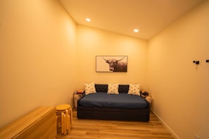 Un dormitorio con cama, almohadas, un cuadro en la pared, una mesita de noche y una pequeña mesa de madera con sillas.