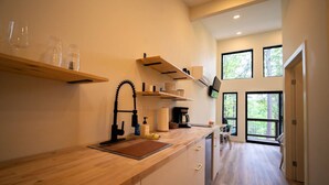 Una cocina moderna con encimeras de madera, un grifo negro y una cafetera. Hay estantes sobre la encimera y un televisor montado en la pared.