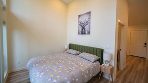 Un dormitorio con una cama, cabecera verde, mesita de noche con lámpara y una obra de arte en la pared con un ciervo.