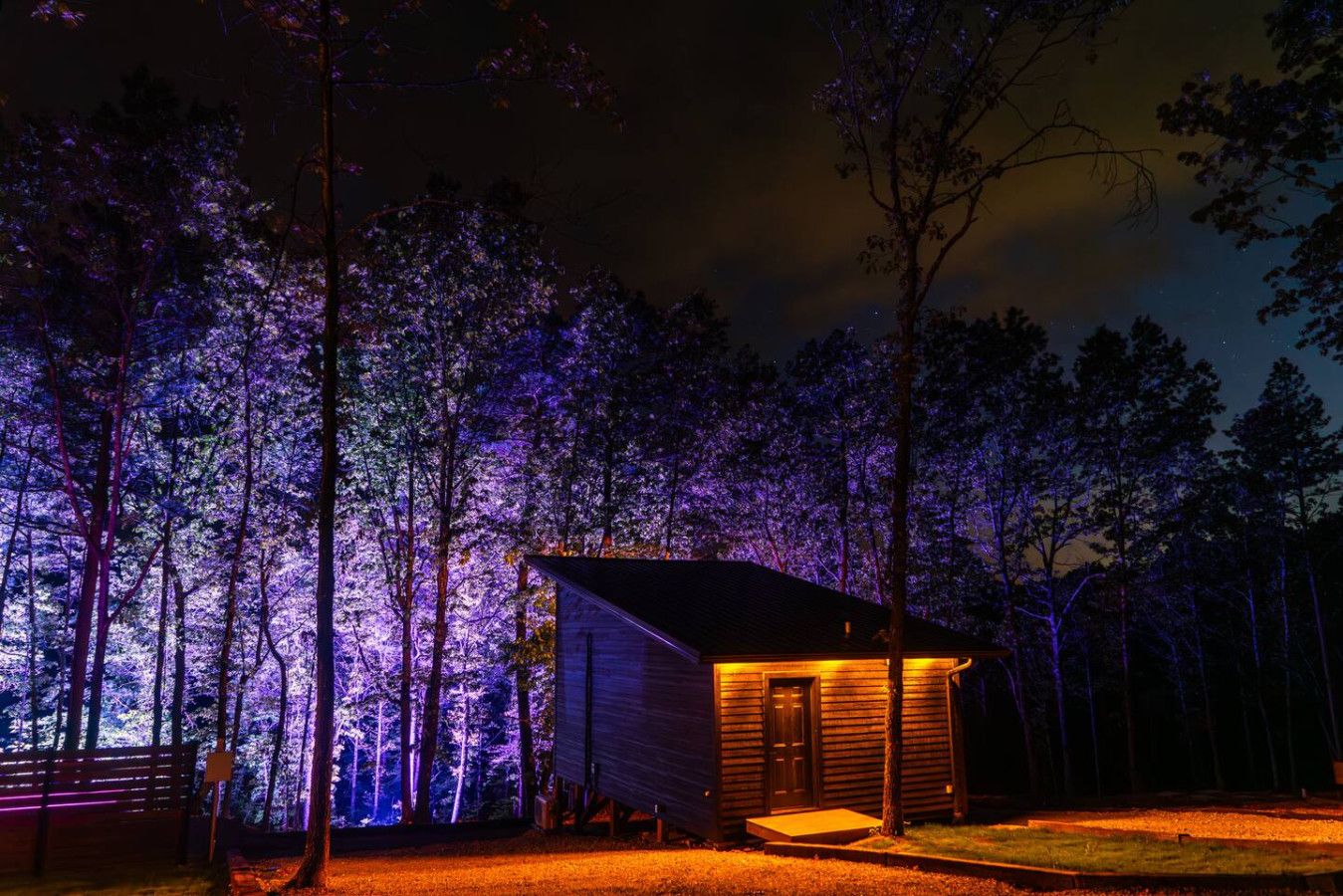 Una piccola baita con facciata in legno e veranda, immersa in una foresta di notte.