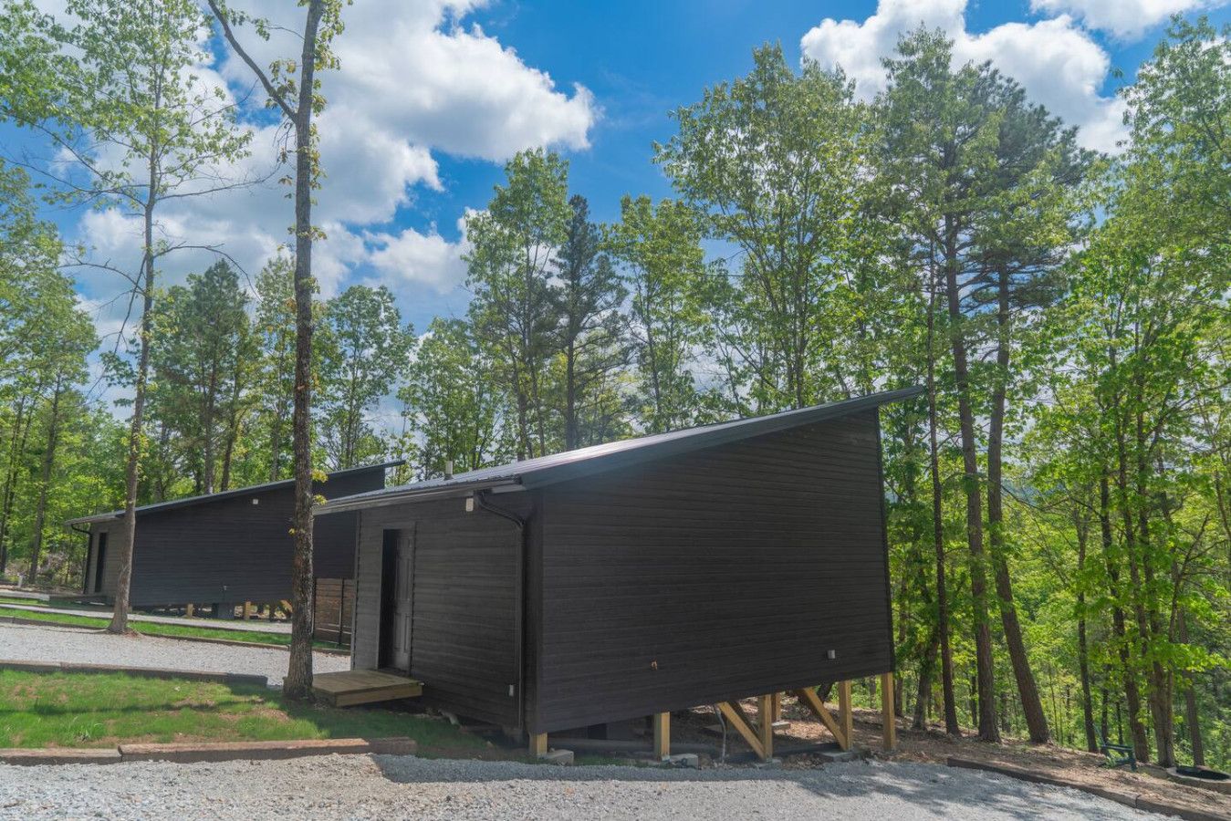 Two wooden cabins in a forest setting with a clear sky.