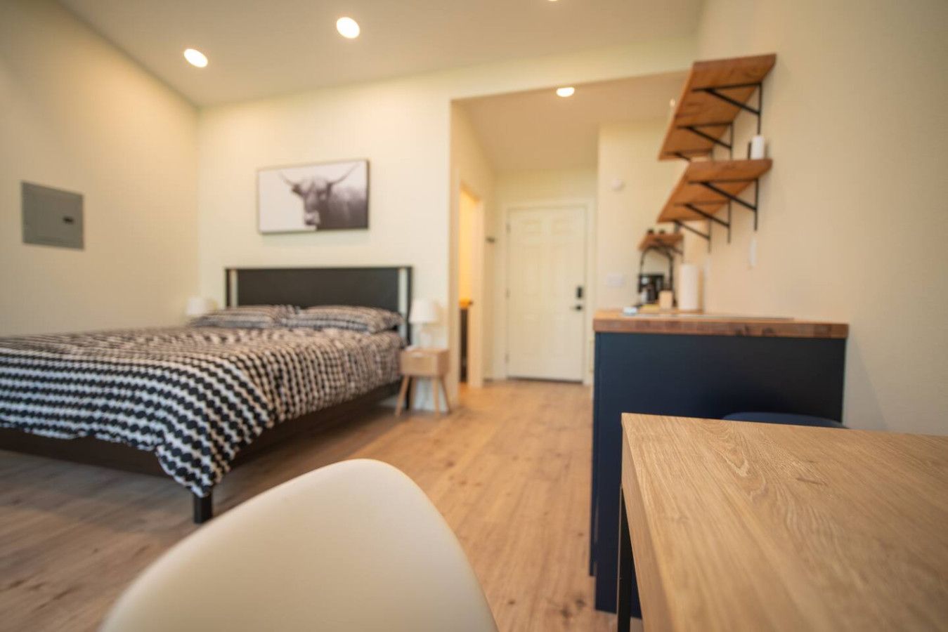 A bedroom with a bed, a desk, and a chair. There is a door leading to another room.