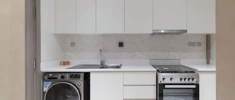 A compact kitchen with a built-in washer and oven, white cabinetry, and a herringbone-patterned backsplash.