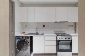 A compact kitchen with a built-in washer and oven, white cabinetry, and a herringbone-patterned backsplash.