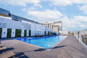 A rooftop swimming pool with lounge chairs and a modern building in the background.