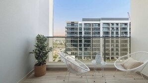 A balcony with a view of a modern building, two white chairs, a small table, and a potted plant.