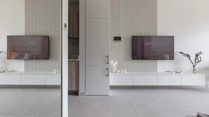 A modern living room with two large flat-screen TVs mounted on a wall with vertical paneling. There is a white console table with decorative items and a small plant.