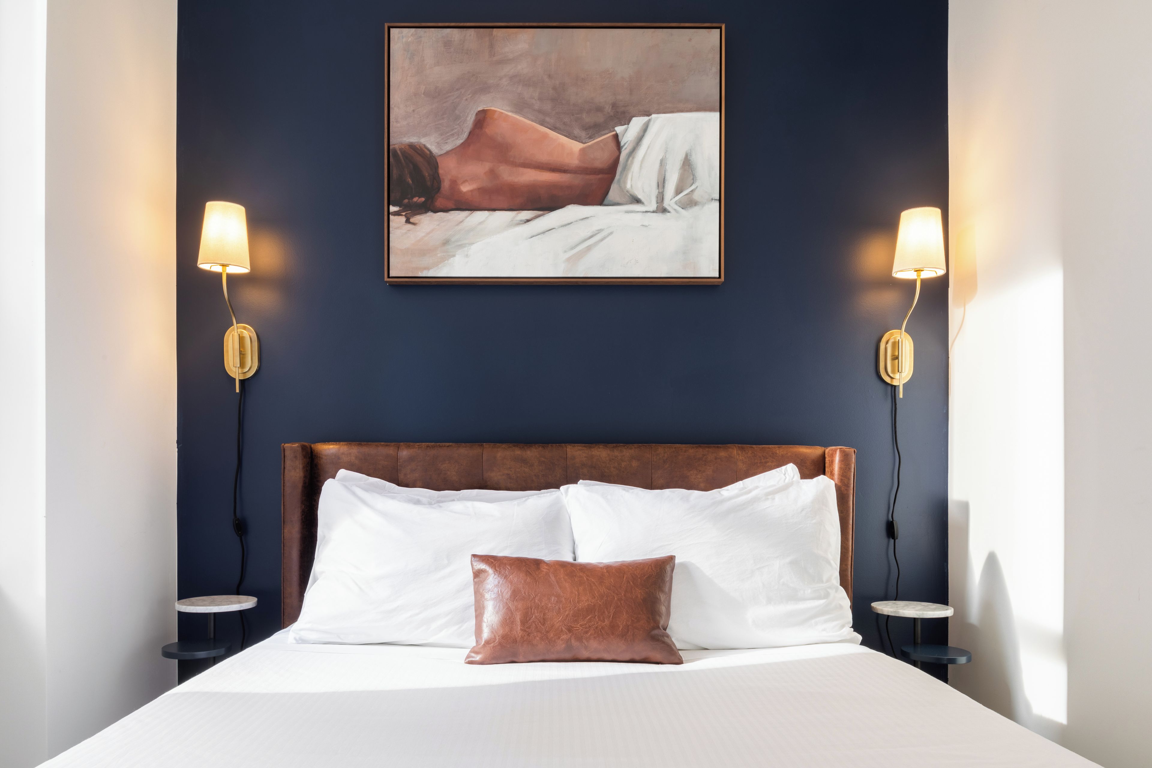 Ein Schlafzimmer mit einem großen Bett, zwei Nachttischlampen, einem gerahmten Kunstwerk über dem Bett und einem kleinen Tisch neben dem Bett.