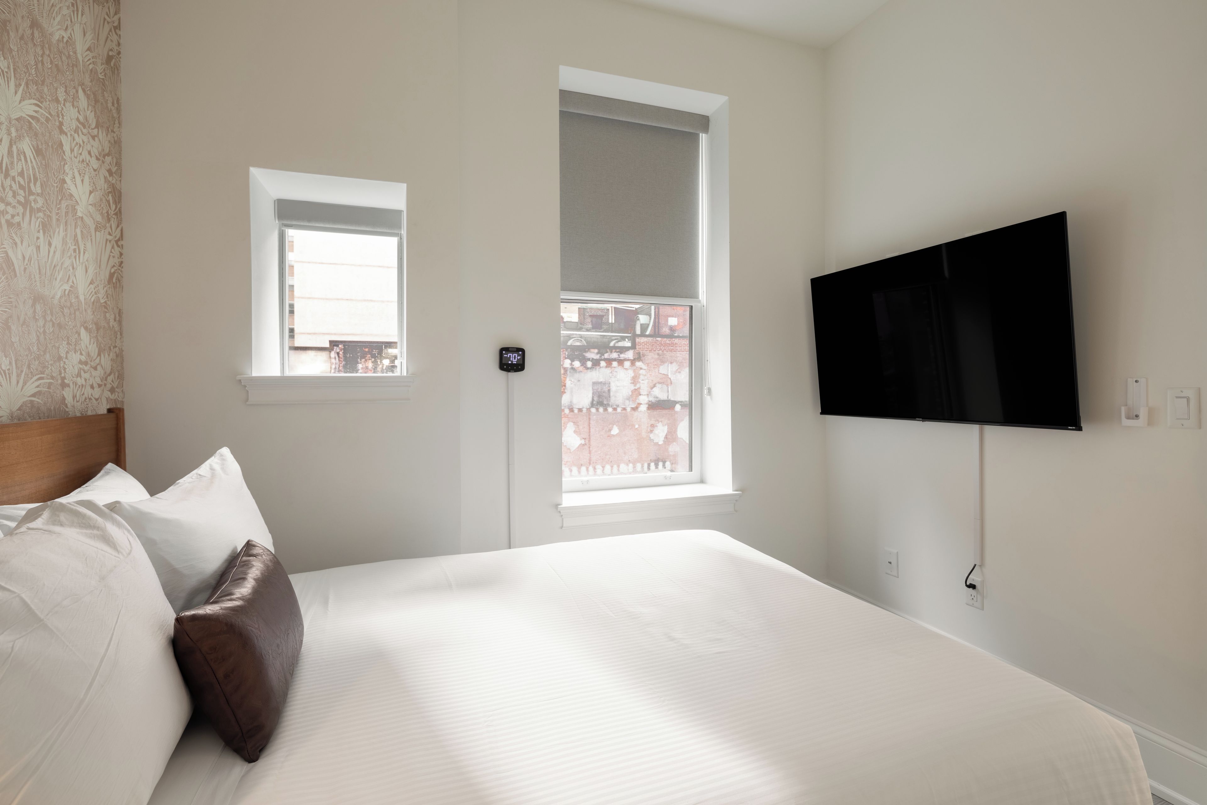 Ein Schlafzimmer mit einem Bett, einem an der Wand befestigten Fernseher und zwei Fenstern.