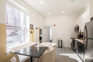 A modern kitchen with a dining area, stainless steel appliances, and a view of the city through large windows. - Sosuite | 1BR Apt w W/D, Large Dining Seating (Philadelphia)