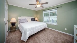 A bedroom with a bed, two bedside lamps, a ceiling fan, a window with blinds, and a carpeted floor. - 4BR Home | Firepit + Yard | Near Historic Downtown (St. Augustine)