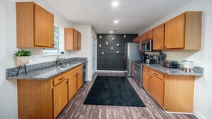 A modern kitchen with wooden cabinets, granite countertops, a black rug, and a stainless steel refrigerator.