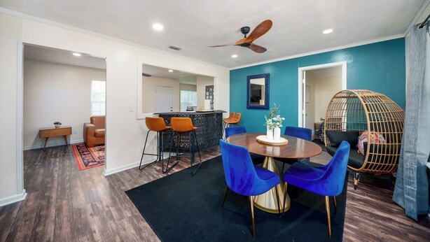 A modern living room with a dining area, a kitchen in the background, and a ceiling fan.