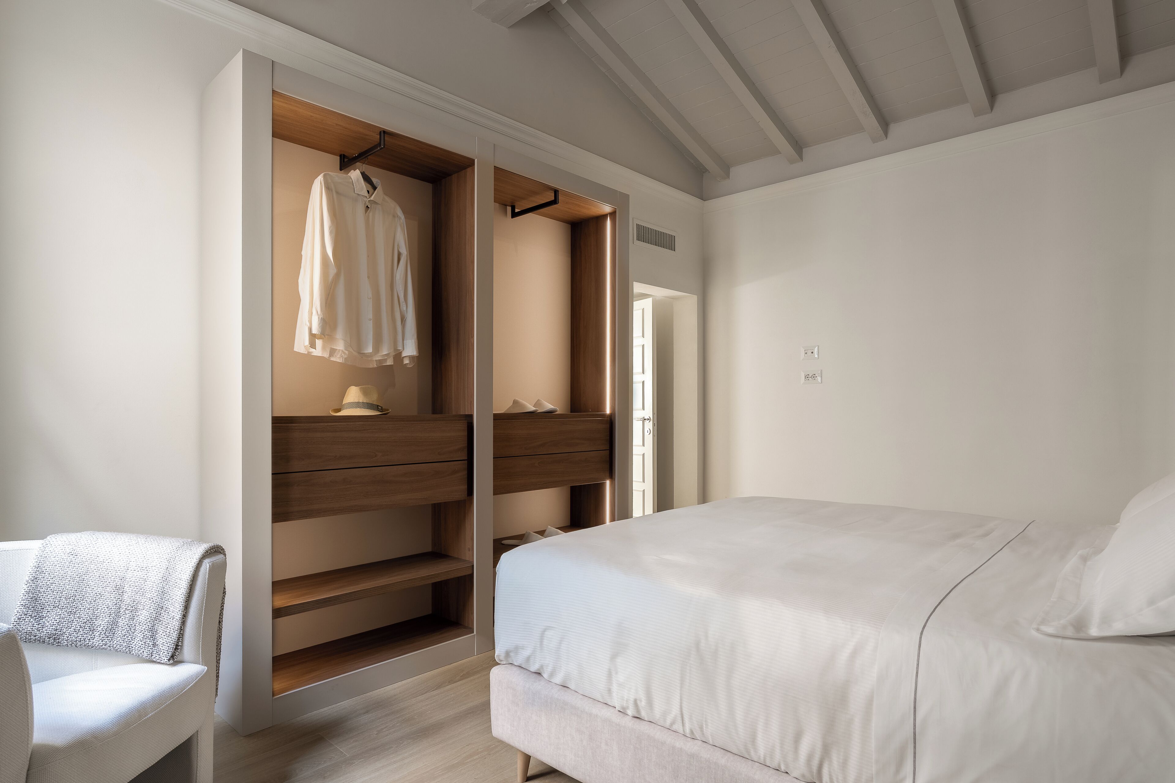 A bedroom with a bed, a chair, and a built-in wardrobe with hanging space.