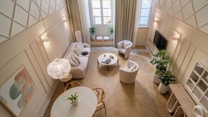 Una sala de estar moderna con un sofá, sillones, una mesa de centro y una mesa de comedor. Hay plantas en macetas y un televisor montado en la pared.
