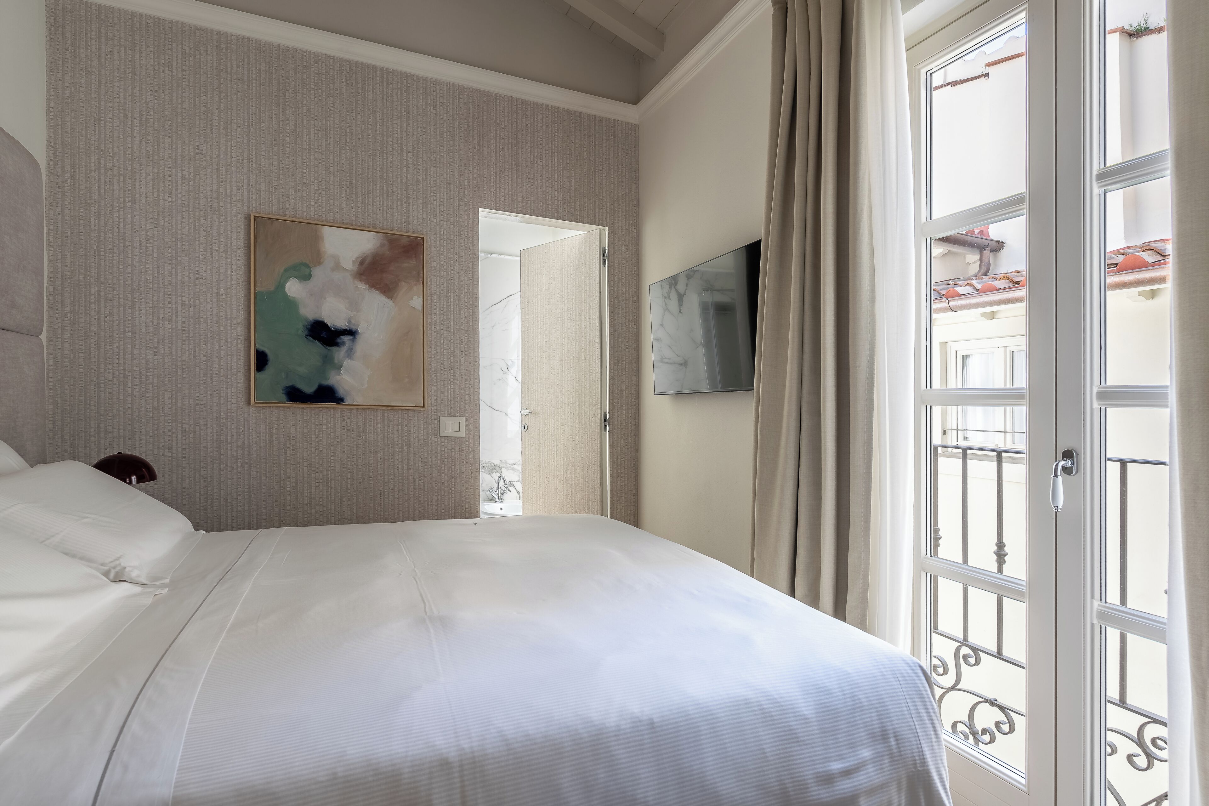 Habitación de hotel con una cama grande, un cuadro en la pared, un televisor y un balcón con vistas.