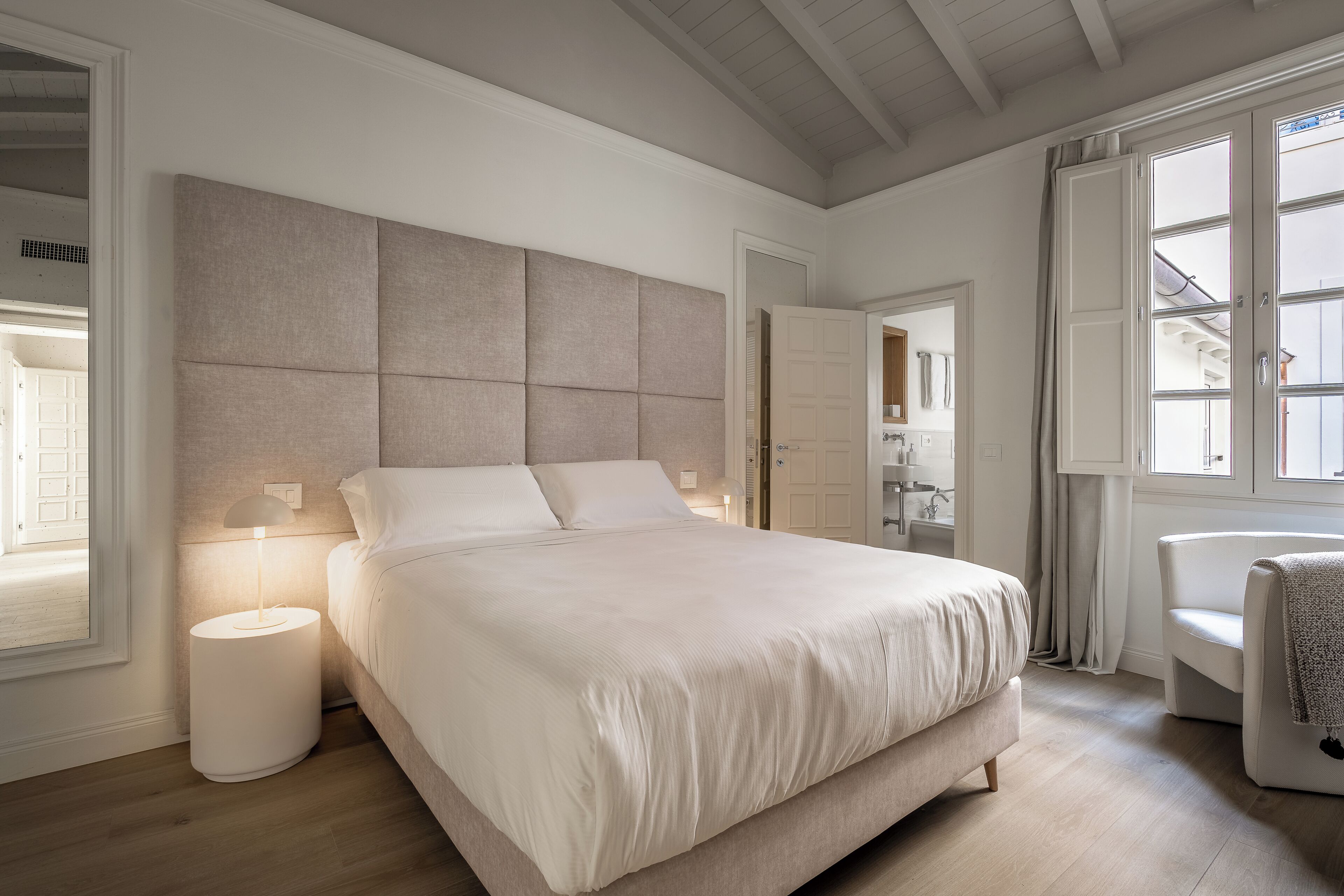 A bedroom with a large bed, bedside lamps, a chair, and a window.