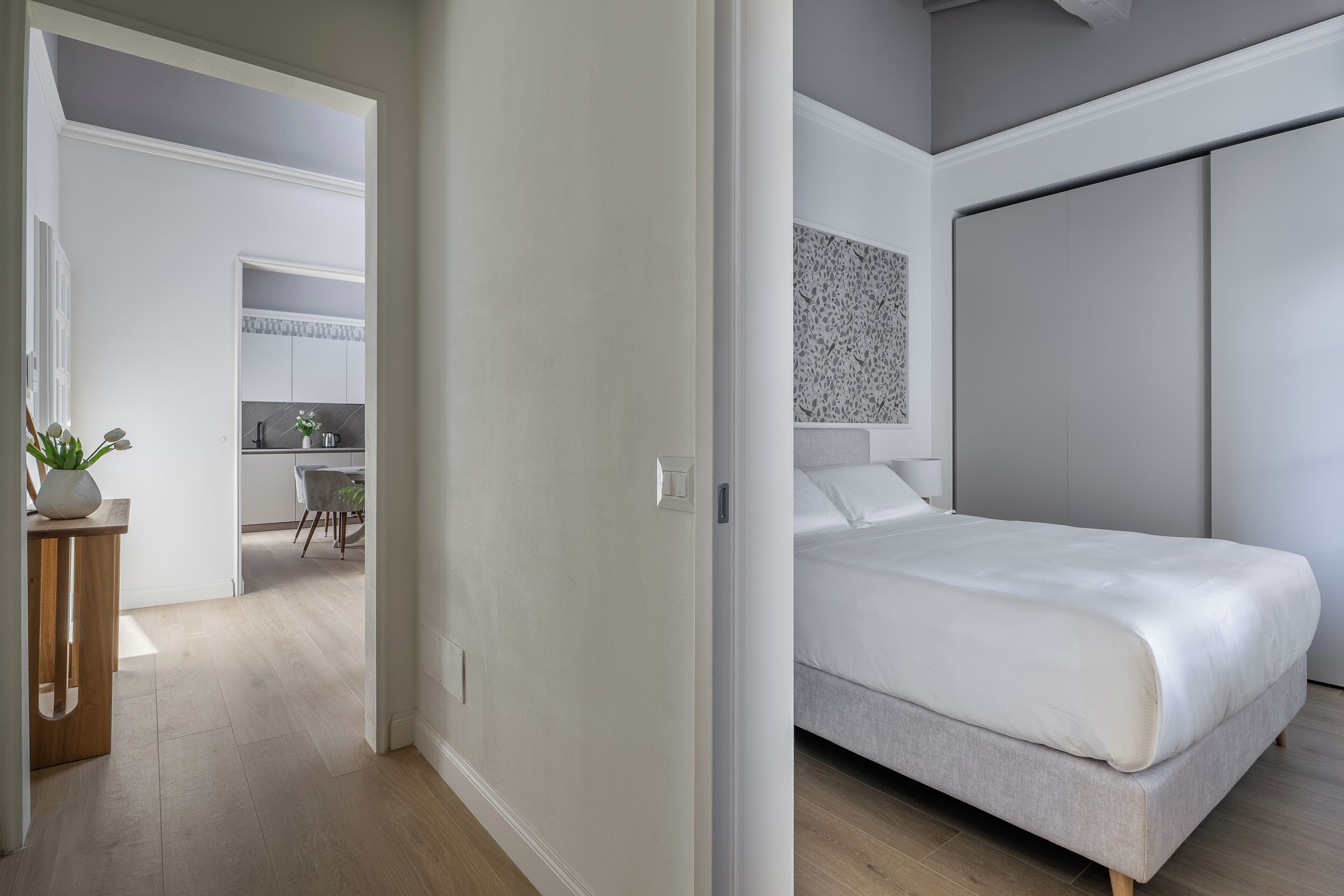A modern bedroom with a bed, a wardrobe, and a view into the kitchen area.