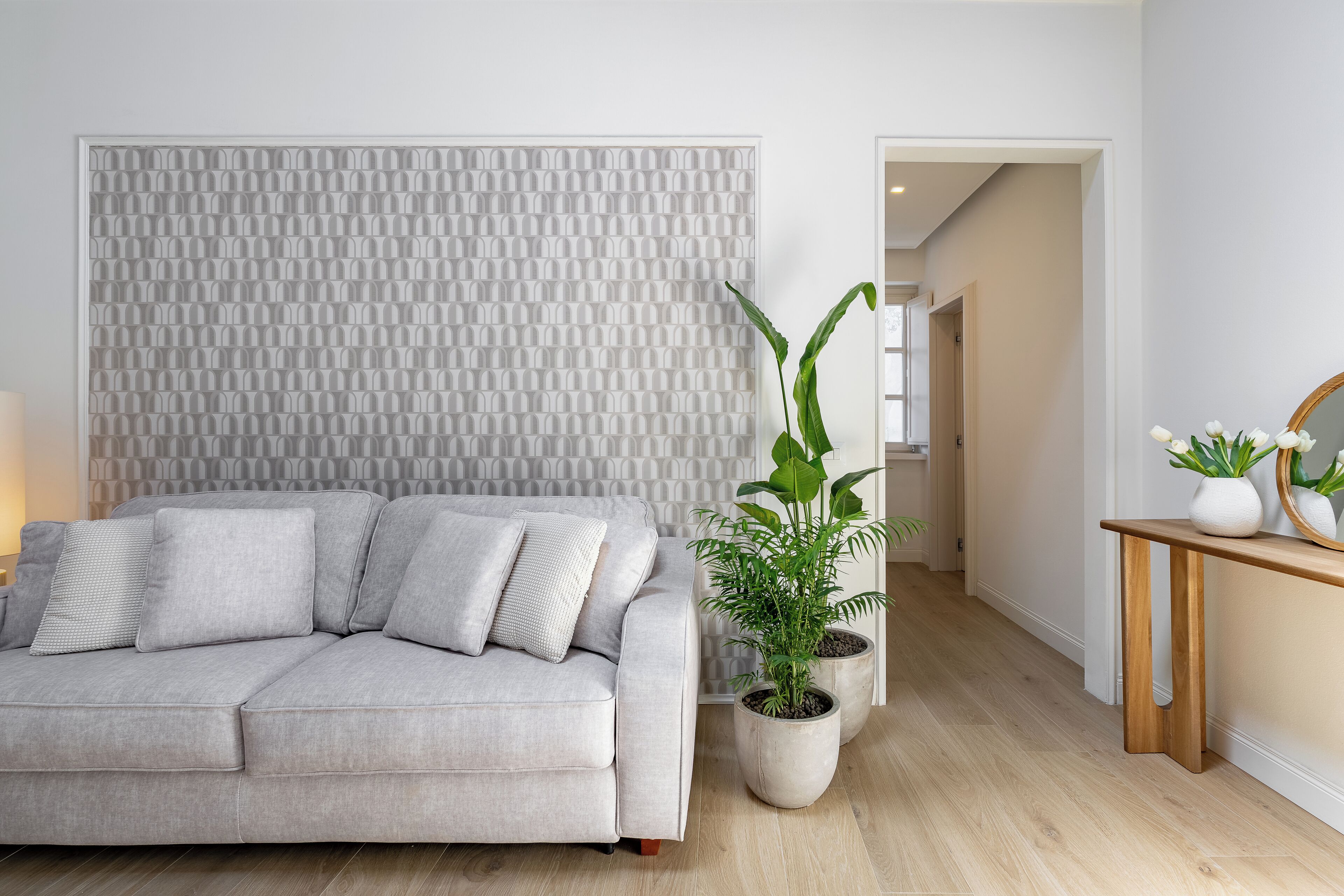 Uma sala de estar moderna com um sofá cinzento, um painel de parede texturizado e duas plantas em vasos.