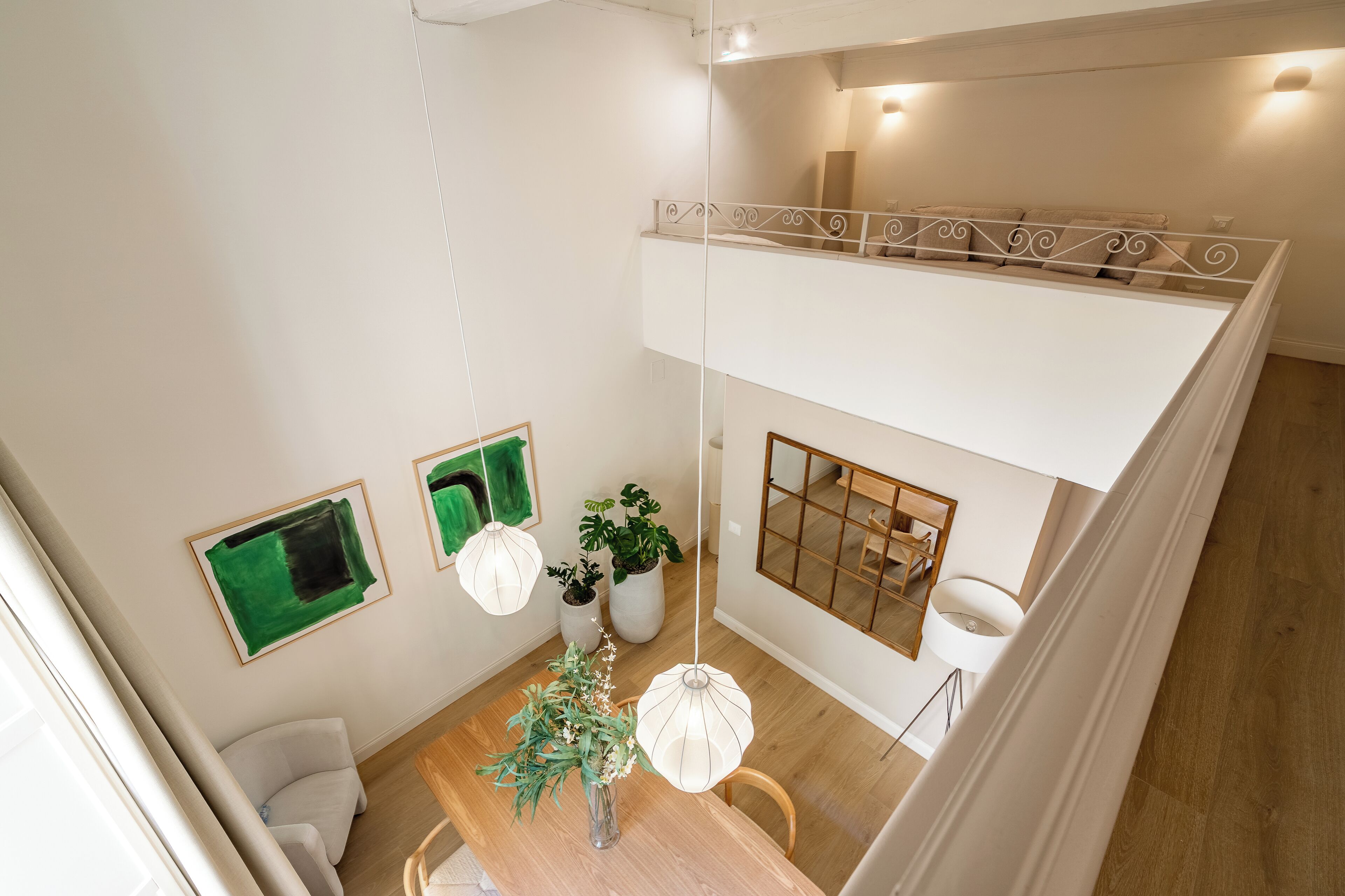 A modern loft-style bedroom with a loft bed, a dining area with a wooden table and chairs, and a view of the living room below.