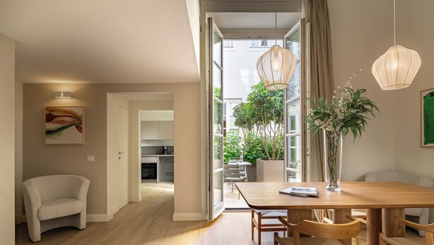 Un comedor moderno con una mesa y sillas de madera, un jarrón con flores y un cuadro en la pared.