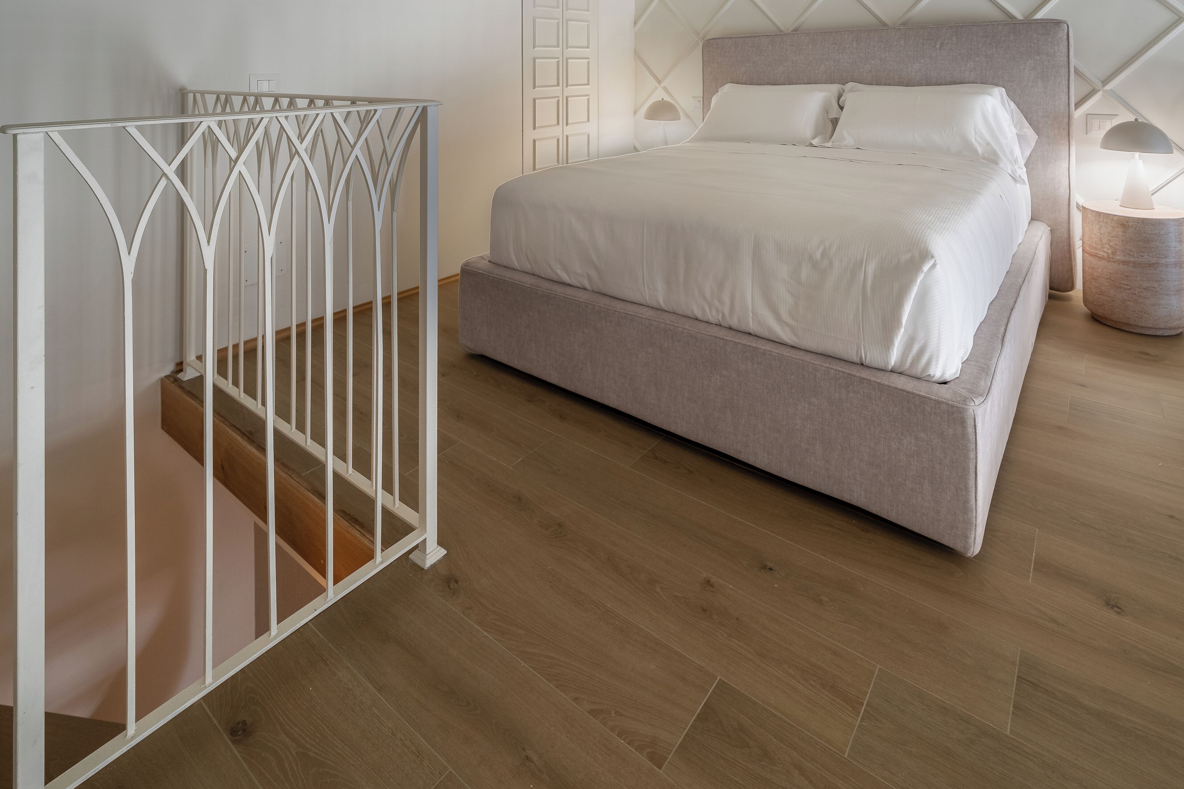 A bedroom with a bed, a nightstand, a lamp, and a white crib.