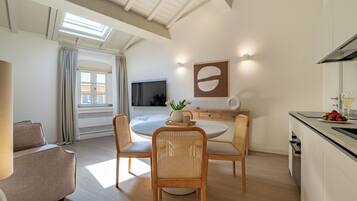 A modern living room with a round dining table, wicker chairs, a sofa, and a kitchen area with a dining table and chairs.