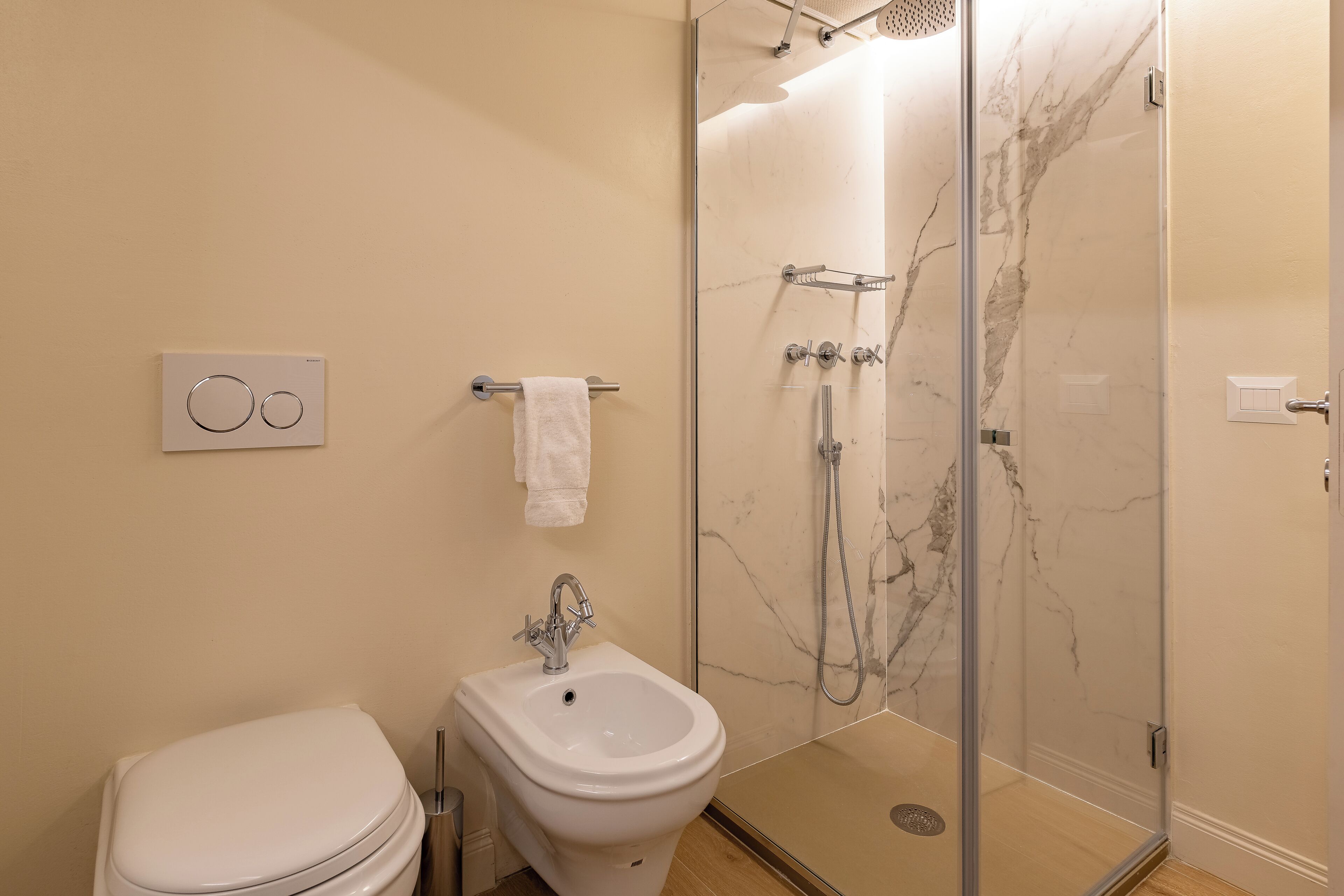 Une salle de bain comprenant des toilettes, un bidet et une douche en verre avec un mur en marbre.