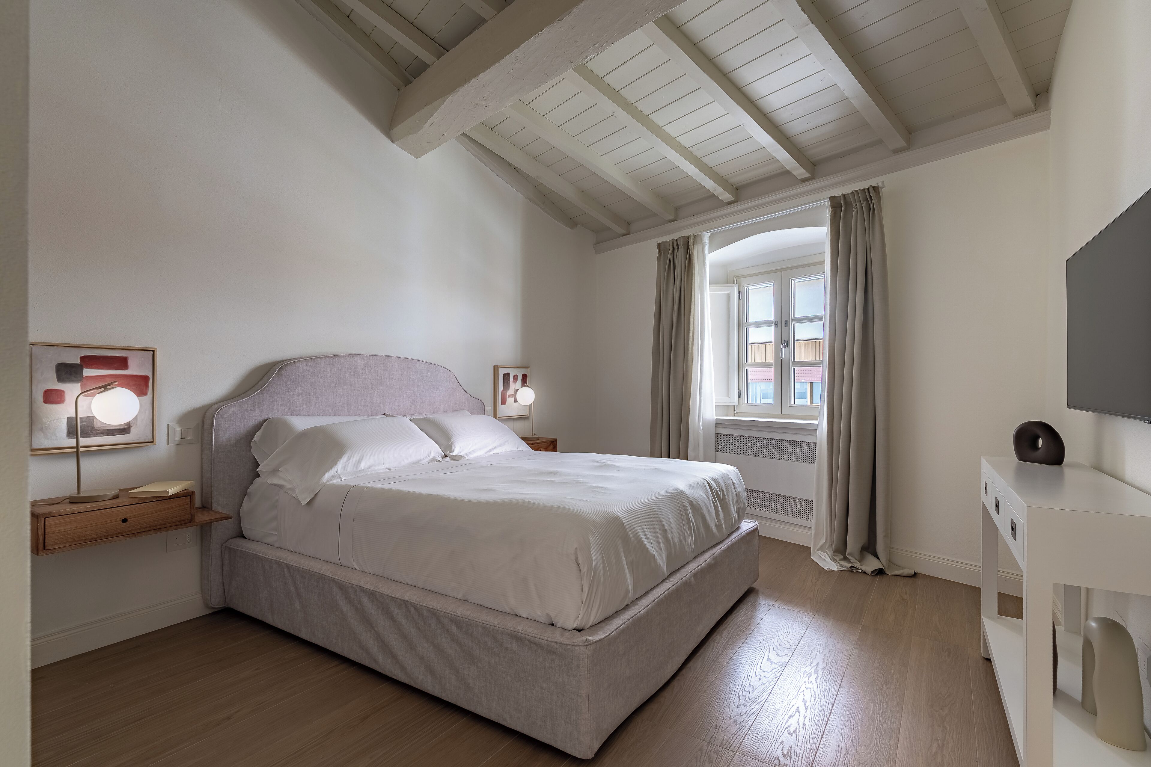 A bedroom with a bed, bedside tables, a desk, and a window with curtains.