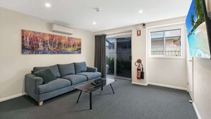 Una sala de estar moderna con un sofá gris, una mesa de centro de vidrio y un cuadro colorido en la pared.