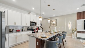 A modern kitchen with white cabinets, stainless steel appliances, and a central island with bar stools. - Ultimate Harry Potter Bunks! Mario & Mickey Resort Near Disney! (Kissimmee)