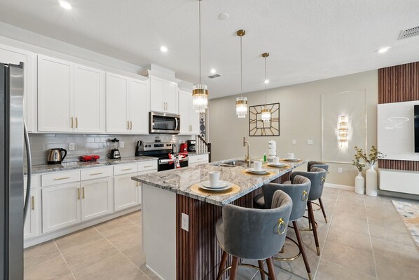 A modern kitchen with white cabinets, stainless steel appliances, and a central island with bar stools. - Magical Harry Potter & Mickey Theme • Mario Kart Loft • Splash Pool • Nr Disney (Kissimmee)