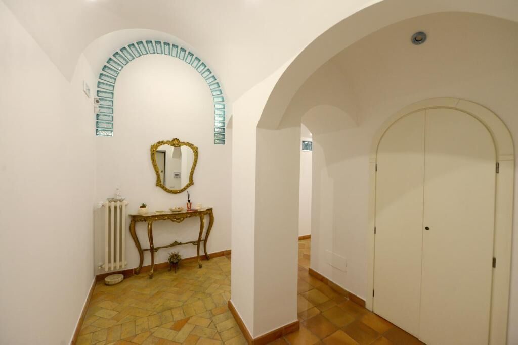 A hallway with an arched doorway, a radiator, a small table with a mirror, and a tiled floor.