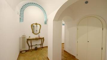 A hallway with an arched doorway, a radiator, a small table with a mirror, and a tiled floor.